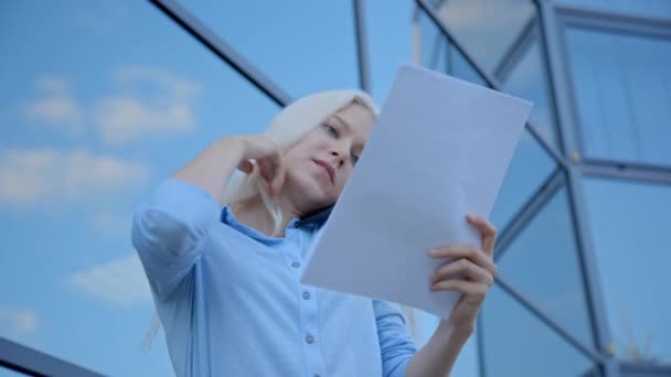 biznes blond kobieta patrząc dokumenty na arkuszach papieru i rozmawia przez telefon - Materiał filmowy, wideo
