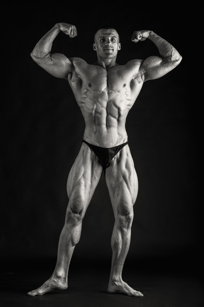 Fisiculturista posando em diferentes poses demonstrando seus músculos. Falha num fundo escuro. Homem mostrando músculos se esforçando. Bonito atleta corpo muscular
. - Foto, Imagem