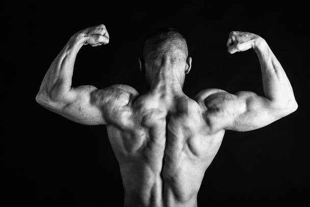 Fisiculturista posando em diferentes poses demonstrando seus músculos. Falha num fundo escuro. Homem mostrando músculos se esforçando. Bonito atleta corpo muscular
. - Foto, Imagem