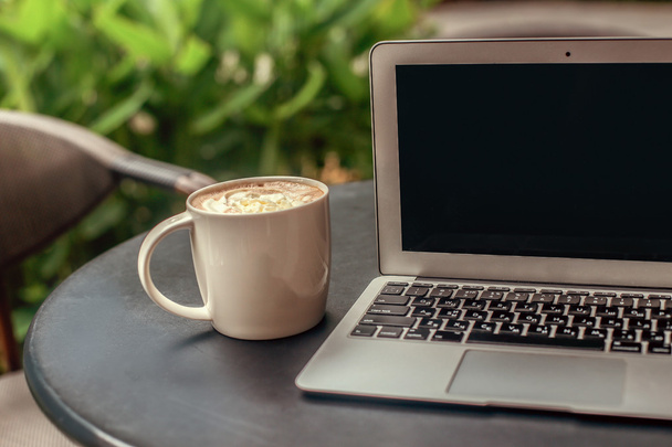 Laptop and cup of coffee on round black table in cafe - Photo, image