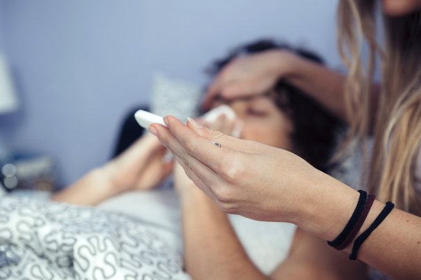 Женщина смотрит температура больного мужчины в термометре
 - Фото, изображение