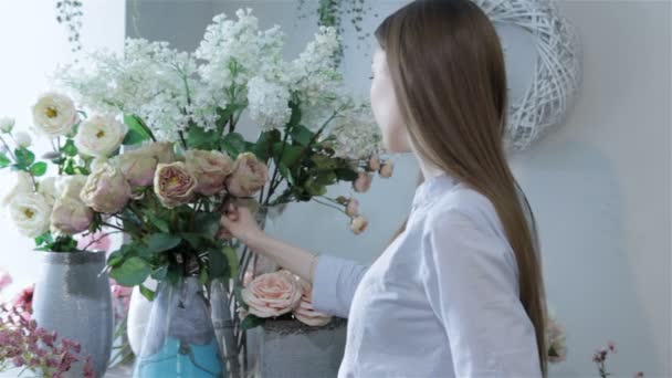 Female florist arranges flowers in vases at flower shop - Záběry, video