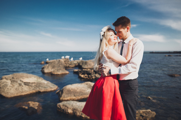 Romantic loving couple posing on stones near sea, blue sky - Фото, изображение