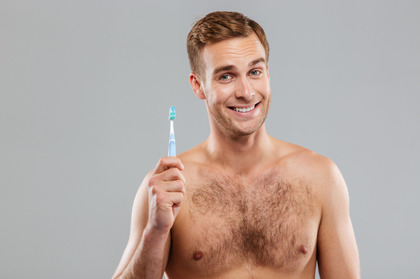 Happy man holding toothbrush on gray background - 写真・画像