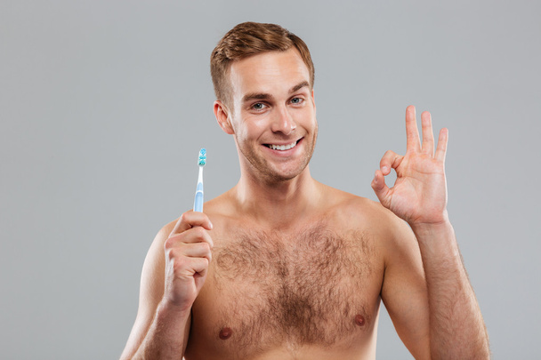 Happy young man holding toothbrush and showing ok sign - Foto, Imagen