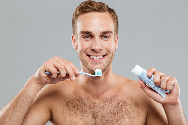 Happy naked young man cleaning teeth with toothbrush and toothpaste - Zdjęcie, obraz