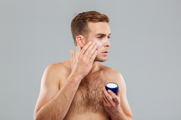 Young man putting cream lotion on face - Фото, зображення