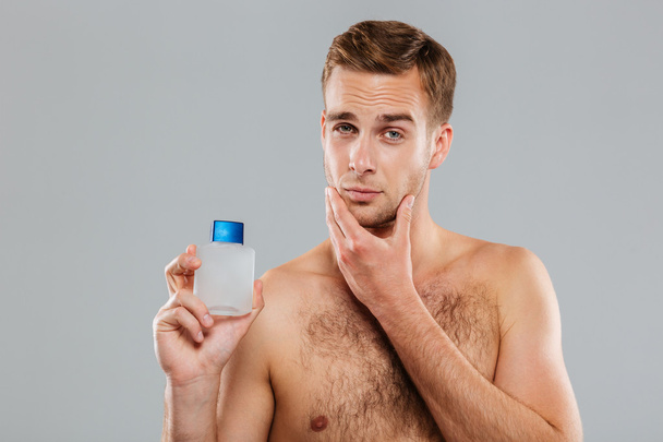 Handsome young man applying lotion after shave on face - Foto, Bild