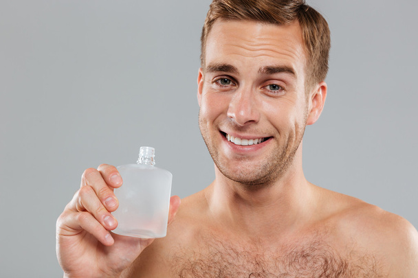Smiling young man applying lotion after shave on face - Foto, Imagem