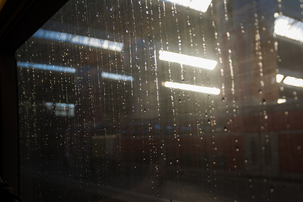 Восход солнца через капли дождя в окне поезда на вокзале
 - Фото, изображение