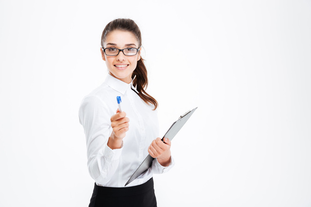 Friendly young smiling businesswoman with clipboard pointing pen at camera - Foto, Bild