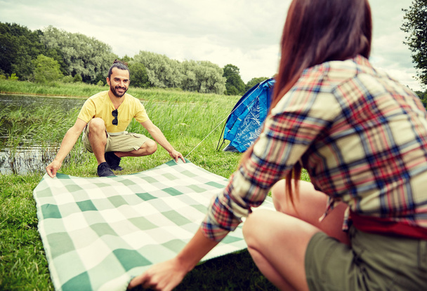 happy couple laying picnic blanket at campsite - Foto, imagen