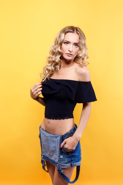 Beautiful blonde model with curly hair posing at camera on yellow studio background - Photo, Image