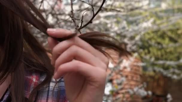 Zbliżenie: brunetka kobieta gospodarstwa i Zawijanie niektóre włosy w jej palce, na zewnątrz - Materiał filmowy, wideo