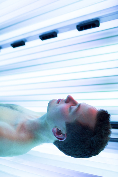 Handsome young man relaxing during a tanning session in a  solarium - Photo, Image