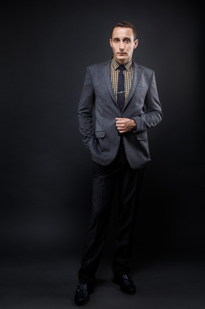 Serious business man brown hair with expressive face wearing grey suit and tie. Isolated on dark background. - Foto, Imagen