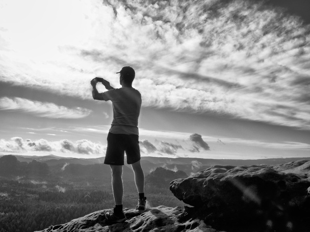 Mann in T-Shirt und Shorts fotografiert mit Smartphone auf Gipfel des Rock-Imperiums.  - Foto, Bild