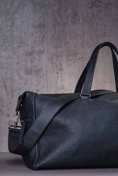 Black leather traveling bag, over the concrete wall background - Foto, imagen