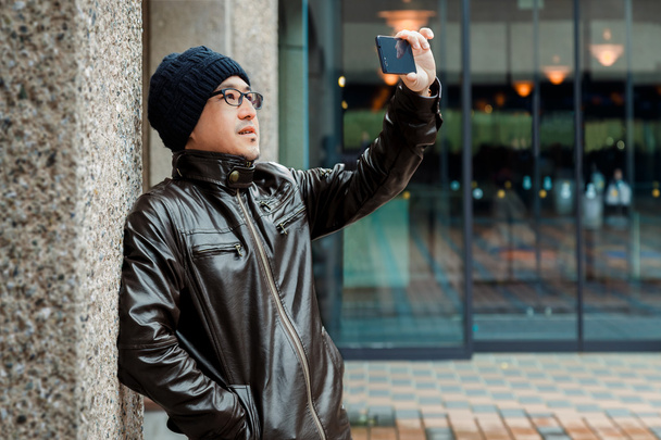 Um homem asiático em uma jaqueta marrom com seu smartphone
 - Foto, Imagem