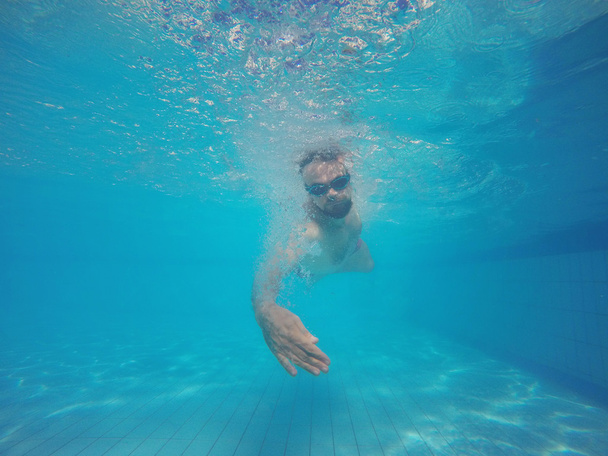 Бородатий чоловік в окулярах плаває під водою в басейні
 - Фото, зображення