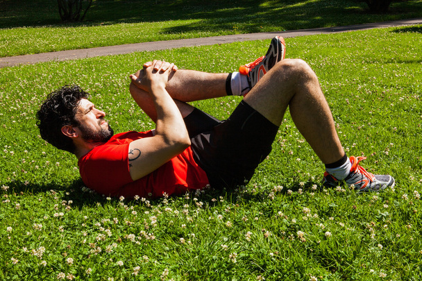 Atleta urbano haciendo ejercicios de estiramiento en la hierba
 - Foto, imagen