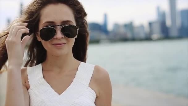 Милая девушка с длинными каштановыми волосами, снимает солнечные очки и показывает свой язык, гуляя по озеру
 - Кадры, видео