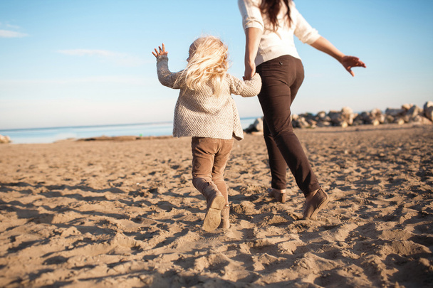VISTA DE VOLTA: A filhinha corre com sua mãe em uma praia
 - Foto, Imagem