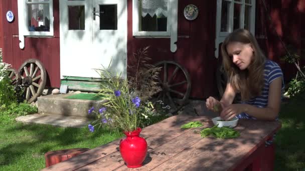 meisje shell erwten aan houten tafel in land met oude huis. 4k - Video
