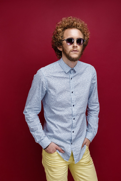 Stylish curly-haired man in sunglasses on red background - Fotó, kép