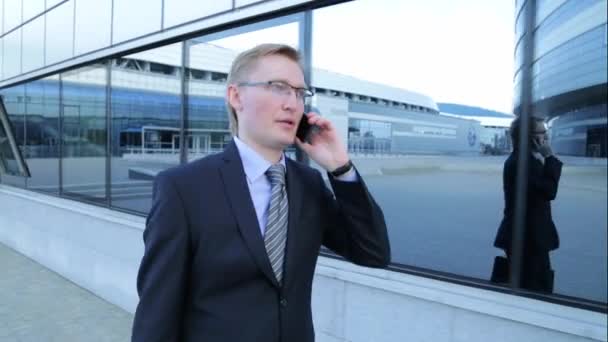 Young businessman is walking and talking on the phone (steadicam shot) - Video