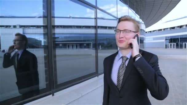 Young businessman is walking and talking on the phone (steadicam shot) - Imágenes, Vídeo