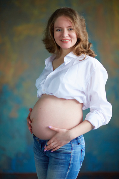 Zwangere vrouw in spijkerbroek in studio - Foto, afbeelding