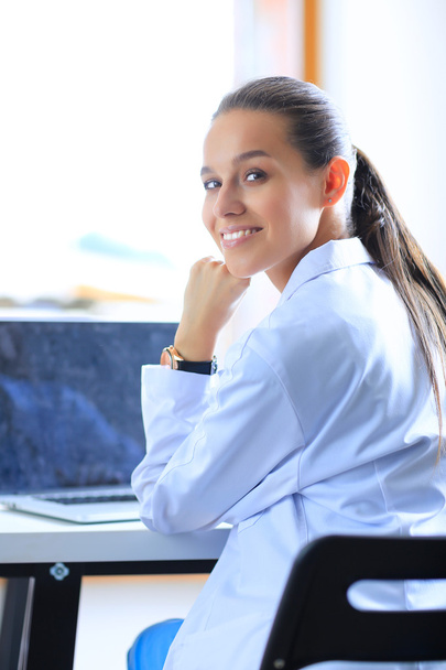 Beautiful young smiling female doctor sitting at the desk - Photo, image