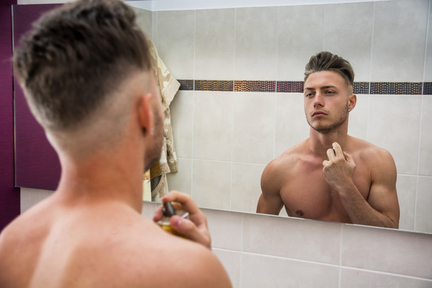 Handsome young man in bathroom, spraying cologne - 写真・画像