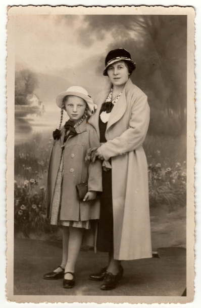 Vintage photo shows woman wears ladies hat (cloche hat) and her daughter. Retro black & white studio photography. - Photo, Image