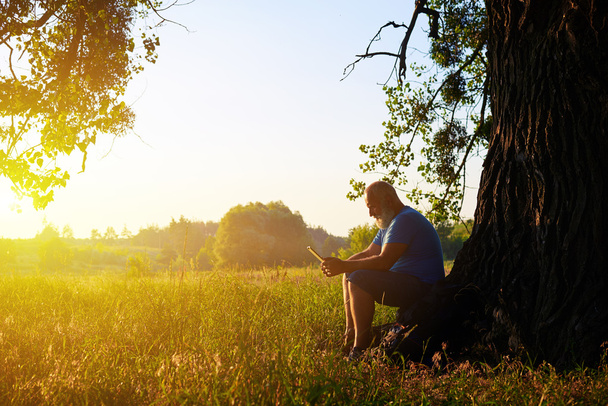 Літня людина під деревом на тлі заходу сонця в полі
 - Фото, зображення