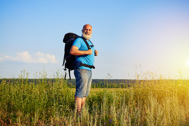 Porträt eines alten Mannes mit Rucksack, der auf einem Feld steht - Foto, Bild