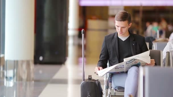 Молодой кавказский человек с газетой в аэропорту в ожидании посадки. Случайный молодой бизнесмен в пиджаке
. - Кадры, видео