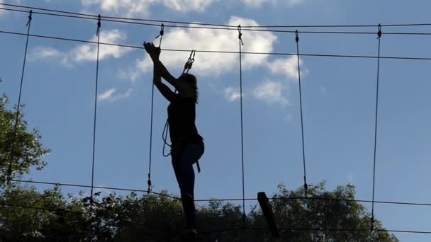 Girl on High Altitude Goes Through the Ropes. Entretenimiento en el parque de cuerdas
. - Imágenes, Vídeo