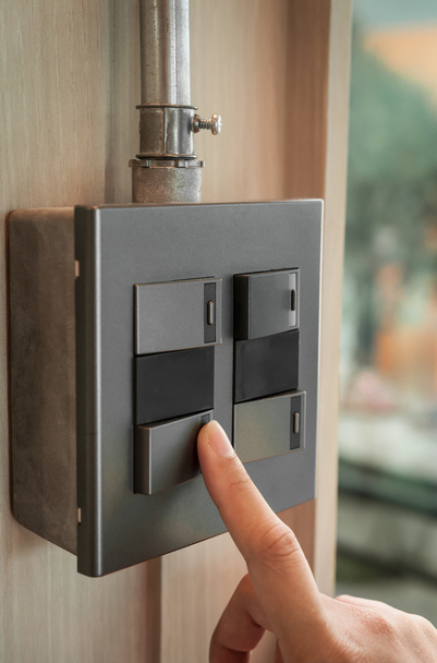 Finger is turning on a grey or black metallic light switch - Photo, image