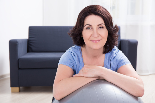 Portrait d’une femme mature sportive avec ballon de fitness à la maison - Photo, image