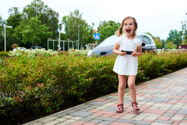 Adorable expressive little girl with a smartphone outdoors - Zdjęcie, obraz