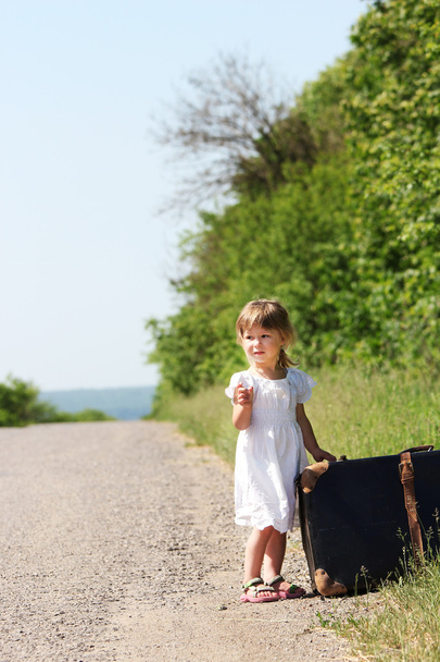 Beautiful little girl by the road with a suitcase - Photo, Image