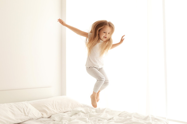 Cute little girl jumping on white bed - 写真・画像