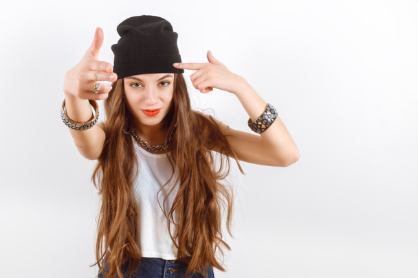 beautiful woman wearing in black hat and white T-shirt standing near white wall, shows the gun fingers of hands - Foto, Bild