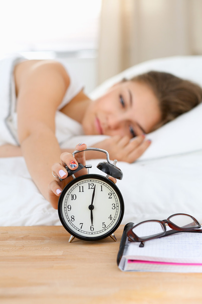 A young woman putting her alarm clock off in the morning - Foto, Imagen
