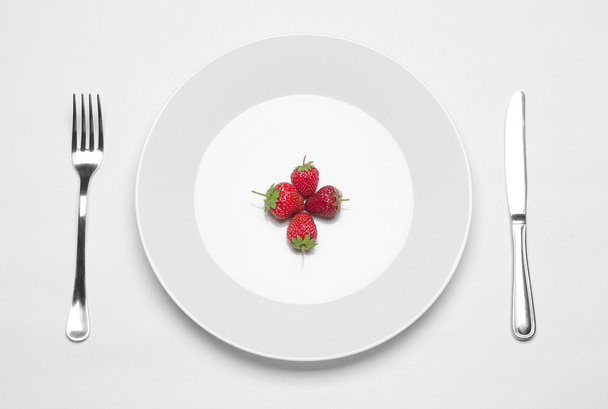 Healthy eating in the restaurant and diet Topic: white plate with three strawberries and a metal knife and fork lying on a white table in the studio isolated top view - Fotoğraf, Görsel