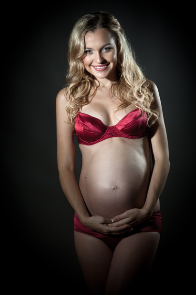 Beautiful pregnant blond woman in red lingerie holding her belly - Foto, imagen