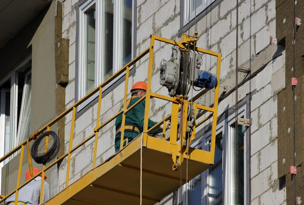 inşaat işçileri ile sarı beşik bir yeni inşa edilen yüksek katlı bina askıya. - Fotoğraf, Görsel