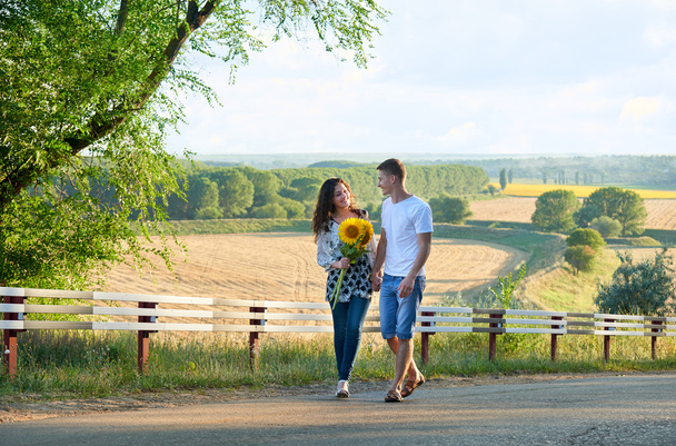 šťastný pár s slunečnice pro zábavu a procházky po venkovské silnici venku - romantické cestování, turistika, cestovní ruch a lidé koncept - Fotografie, Obrázek